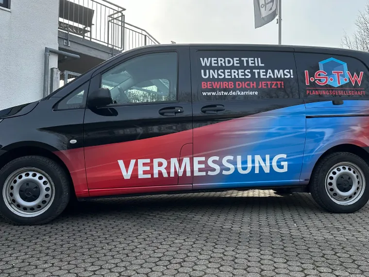Dunkler ISTW-Transporter mit roter Vermessung-Beschriftung und Mitarbeitersuche auf der Seitenfläche